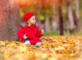 Happy caucasian little girl in a red coat and beret in the park with a red apple sitting near a tree Royalty Free Stock Photo