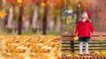 Happy caucasian little girl in a red coat and beret in the park with a red apple sitting near a tree Royalty Free Stock Photo