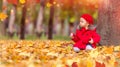 Happy caucasian little girl in a red coat and beret in the park with a red apple sitting near a tree Royalty Free Stock Photo