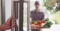 Happy caucasian male deliverer with box of vegetables opening door