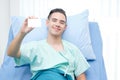 Happy Caucasian man patient holding mock up blank white card on hospital bed