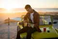 Happy caucasian man sitting on beach buggy by the sea playing guitar during sunset Royalty Free Stock Photo