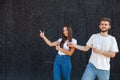 A happy Caucasian man and woman pointing with fingers to the left at the copy space and standing in white T-shirts Royalty Free Stock Photo