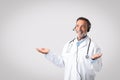 Happy caucasian mature man doctor therapist in white coat, headphones spreads arms to sides, hold free space Royalty Free Stock Photo