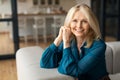 Happy caucasian mature woman sitting on sofa in living room interior, posing looking and smiling at camera, free space Royalty Free Stock Photo