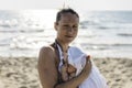 Happy caucasian mother with acne stained skin holding her infant baby girl on the beach in sunny day - Family, skincare, real