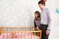 Happy Caucasian parents standing near baby bed and looking at child