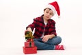 Happy child boy in Santa hat, red plaid shirt and socks with Christmas pattern stacks gifts one on one. White background Royalty Free Stock Photo