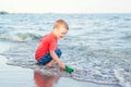 toddler child boy putting green paper boat in water on lake sea ocean shore Royalty Free Stock Photo