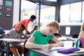 Happy caucasian schoolgirl writing at her desk with diverse pupils and teacher, copy space