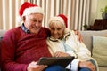 Happy caucasian senior couple having christmas tablet video call embracing in living room