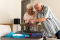 Happy caucasian senior couple packing suitcase and smiling in sunny bedroom at home Royalty Free Stock Photo