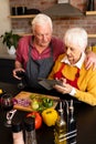 Happy caucasian senior couple preparing vegetables, drinking wine and using tablet in kitchen Royalty Free Stock Photo