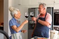 Happy caucasian senior couple standing in kitchen, drinking wine and preparing meal together Royalty Free Stock Photo