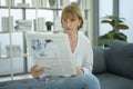 Happy  Caucasian senior woman  is relaxing , reading newspaper in living room Royalty Free Stock Photo