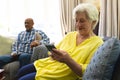 Happy caucasian senior woman sitting on sofa, using smartphone and smiling in sunny living room Royalty Free Stock Photo