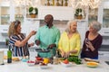 Happy caucasian senior women having wine while friends preparing food together at home Royalty Free Stock Photo