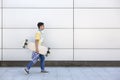 Happy caucasian teenage boy with a long skateboard in his hand walking next to a wall. Urban lifestyle Royalty Free Stock Photo