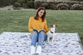 happy caucasian woman having fun with jack russell dog in park, sitting on blanket during autumn season. Woman reading a book Royalty Free Stock Photo