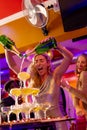 Happy caucasian woman pouring a champagne fountain into glasses with diverse friends at a nightclub