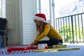 Happy caucasian woman in santa hat sitting on floor and packing gift at christmas at home