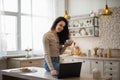 Happy caucasian woman using laptop and drinking tea, sitting on table in kitchen and surfing internet, free space Royalty Free Stock Photo