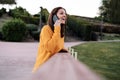 happy caucasian woman wearing yellow pullover talking on mobile phone outdoors in park during sunset. Technology and lifestyle Royalty Free Stock Photo