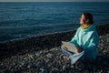 Happy caucasian woman working on a laptop while sitting on a pebble beach.