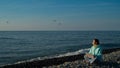 Happy caucasian woman working on a laptop while sitting on a pebble beach.