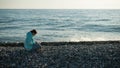 Happy caucasian woman working on a laptop while sitting on a pebble beach.