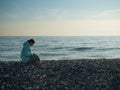 Happy caucasian woman working on a laptop while sitting on a pebble beach.