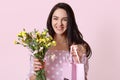 Happy Caucasian young woman with healthy skin, toothy charming smile, recieves presents from husband on Womens Day, holds gift bag