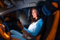 Happy caucasian young woman using smartphone while sitting at passenger front seat of luxury car at night Royalty Free Stock Photo