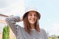 Happy Caucasian young woman wearing panama and striped shirt laughing looking at camera standing on street hipster girl posing Royalty Free Stock Photo