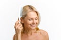 Happy charming 40s 50s middle aged woman combing her blonde well-looking hair, looking away and smiling wide