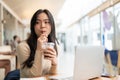 A happy Asian woman enjoying her iced coffee while working remotely at a coffee shop Royalty Free Stock Photo