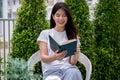 A happy, charming young Asian woman enjoying reading a book in her home garden on a bright day Royalty Free Stock Photo