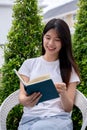 A happy, charming young Asian woman enjoying reading a book in her home garden on a bright day Royalty Free Stock Photo