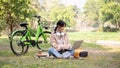 A happy young Asian woman is working remotely in a green park, using her laptop computer Royalty Free Stock Photo