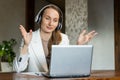 A happy charming young business woman wearing a headset is having a video call on laptop. Young woman in office. Royalty Free Stock Photo