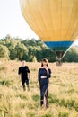 Happy charming young woman in fashionable black clothes, standing in beautiful summer green field, while her boyfriend Royalty Free Stock Photo