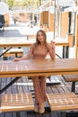 A happy charming young woman is sitting at a table in an outdoor cafe and waiting for her order Royalty Free Stock Photo