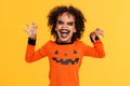 ethnic boy in pumpkin costume and terrible makeup scary make gestures and celebrates Halloween on yellow background