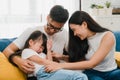 Happy cheerful Asian family dad, mom and daughter having fun cuddling playing on sofa while birthday at house. Self-isolation,