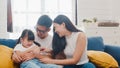 Happy cheerful Asian family dad, mom and daughter having fun cuddling playing on sofa while birthday at house. Self-isolation,