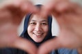 Happy cheerful Asian muslim woman smiling to camera while framing her face with heart shape made with her fingers Royalty Free Stock Photo