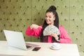 Happy cheerful beautiful young businesswoman with black dreadlocks hairstyle in pink blouse is sitting, holding many dollars, Royalty Free Stock Photo