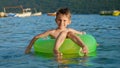 Happy cheerful boy splashing water while sitting in inflatable ring and swimming on calm sea waves at sunset. Family Royalty Free Stock Photo