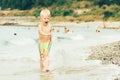 Happy cheerful boy in swimming trunks runs and splashes in the waves along the seashore