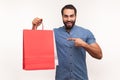 Happy cheerful businessman pointing finger at paper shopping bags in hand, satisfied pleased with shopping, big sale